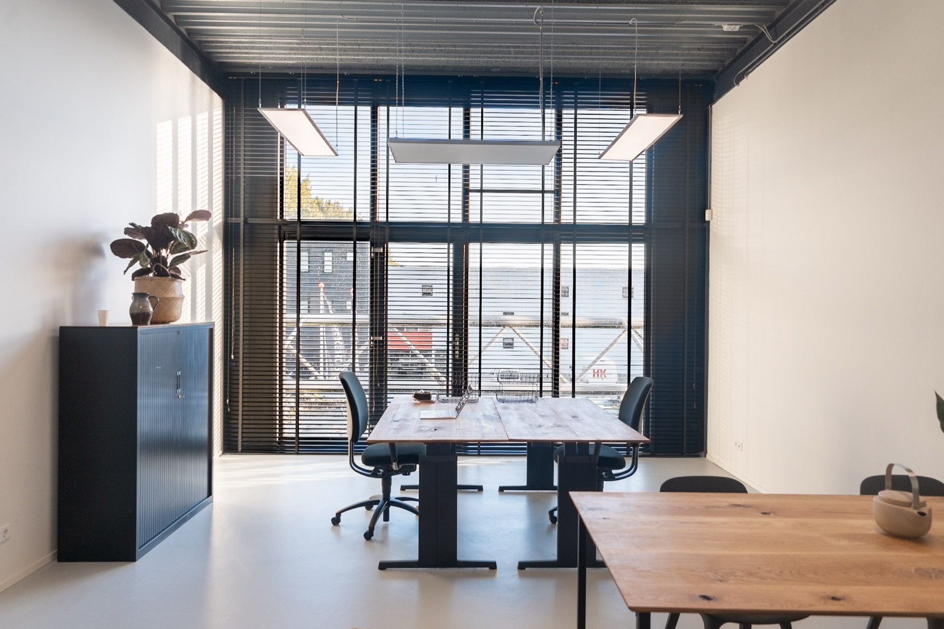 Kantoor L met een wand van hoge ramen, jaloezieën en een lange werktafel